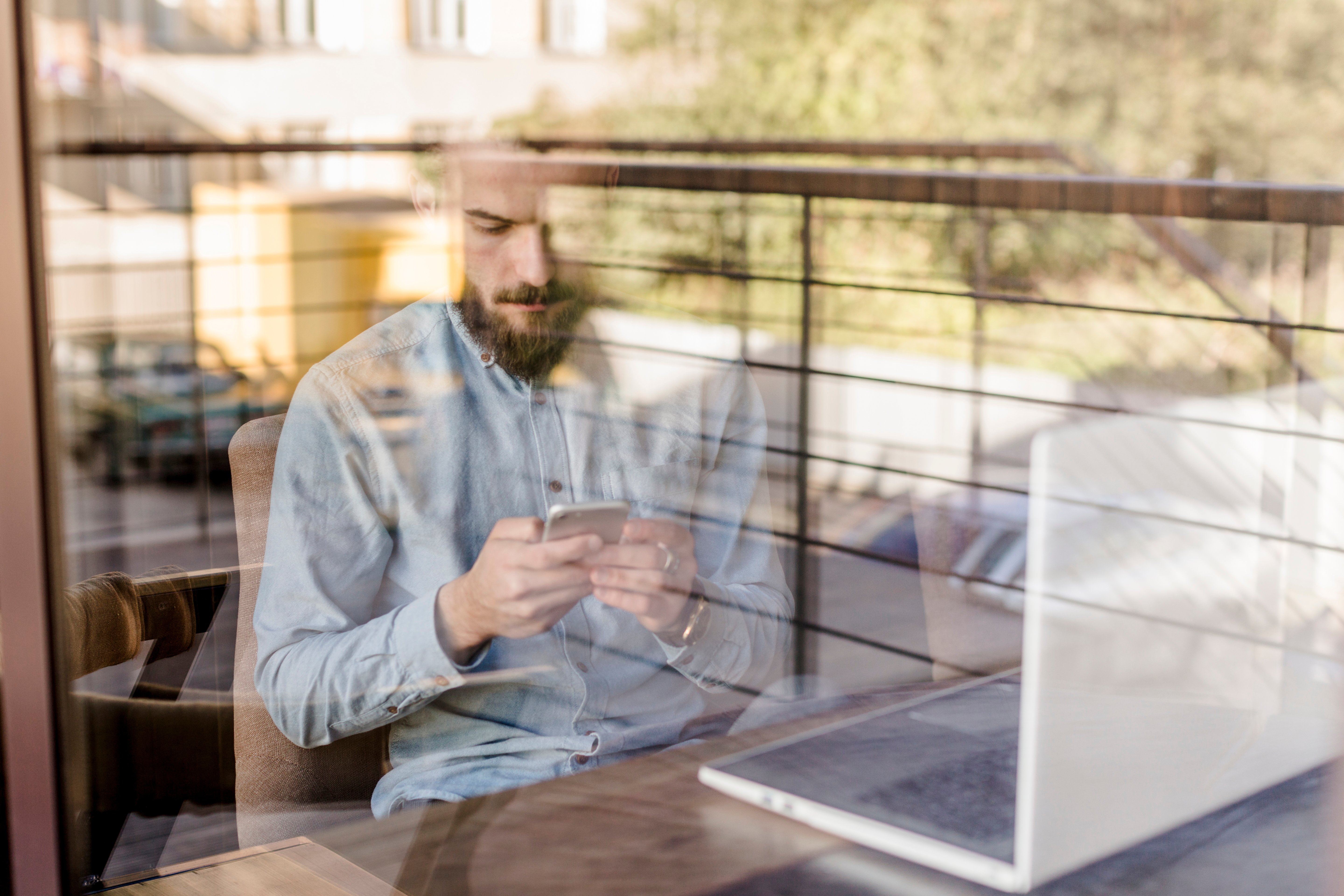 bearded-man-using-mobile-phone-seen-through-transparent-glass-caf